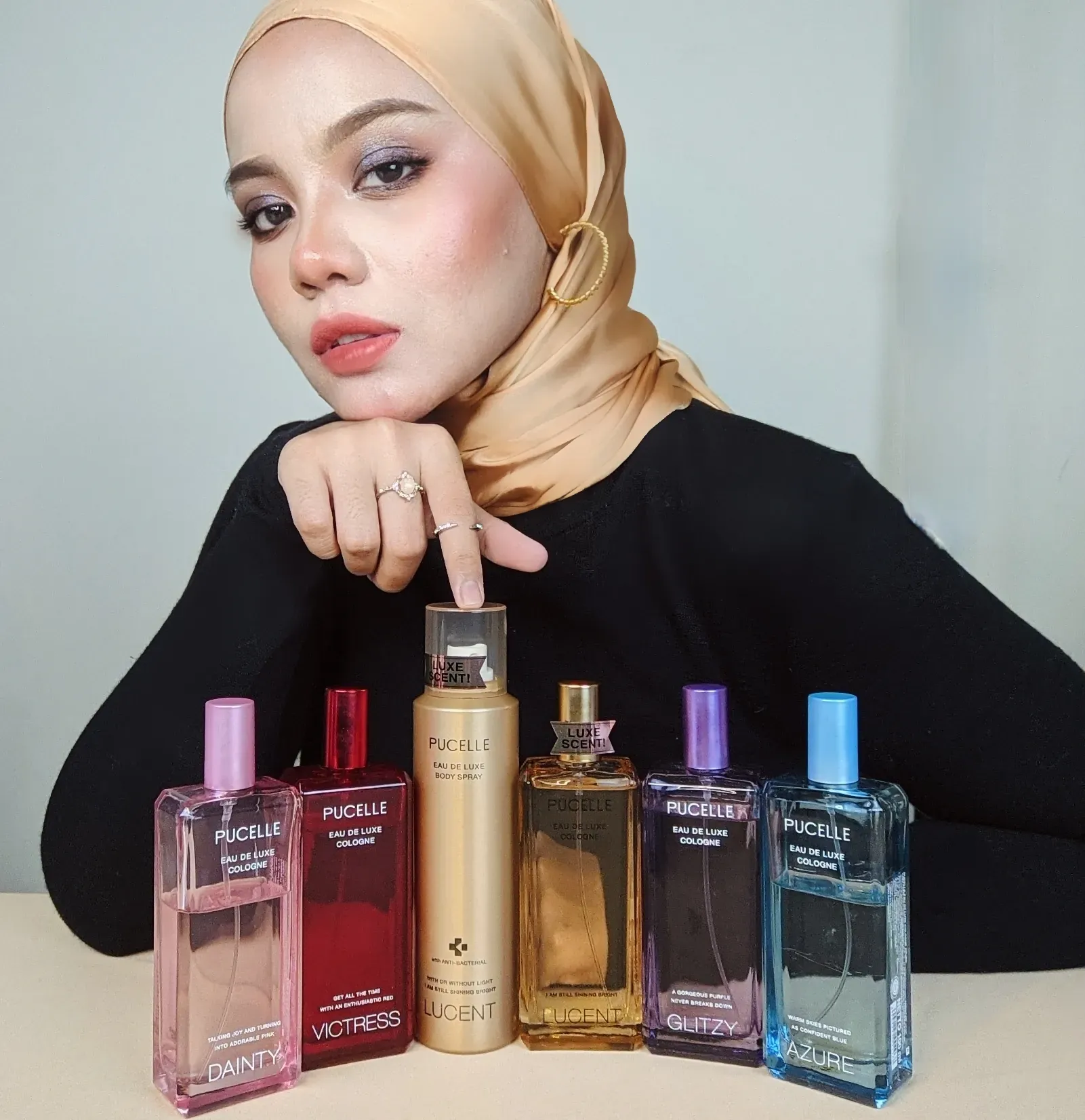 Nabilah in a beige hijab, resting her chin on her hand behind a row of Pucelle fragrance bottles